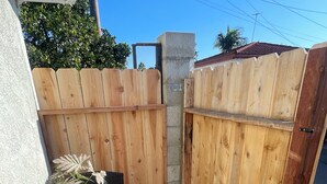 Un pequeño patio al aire libre con una mesa, sillas, una planta en maceta y una valla de madera.