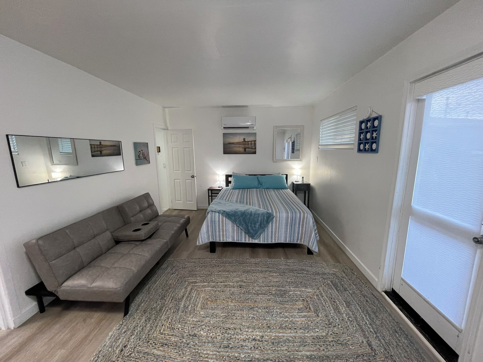A bedroom with a bed, a sofa, a rug, a mirror, and a door.
