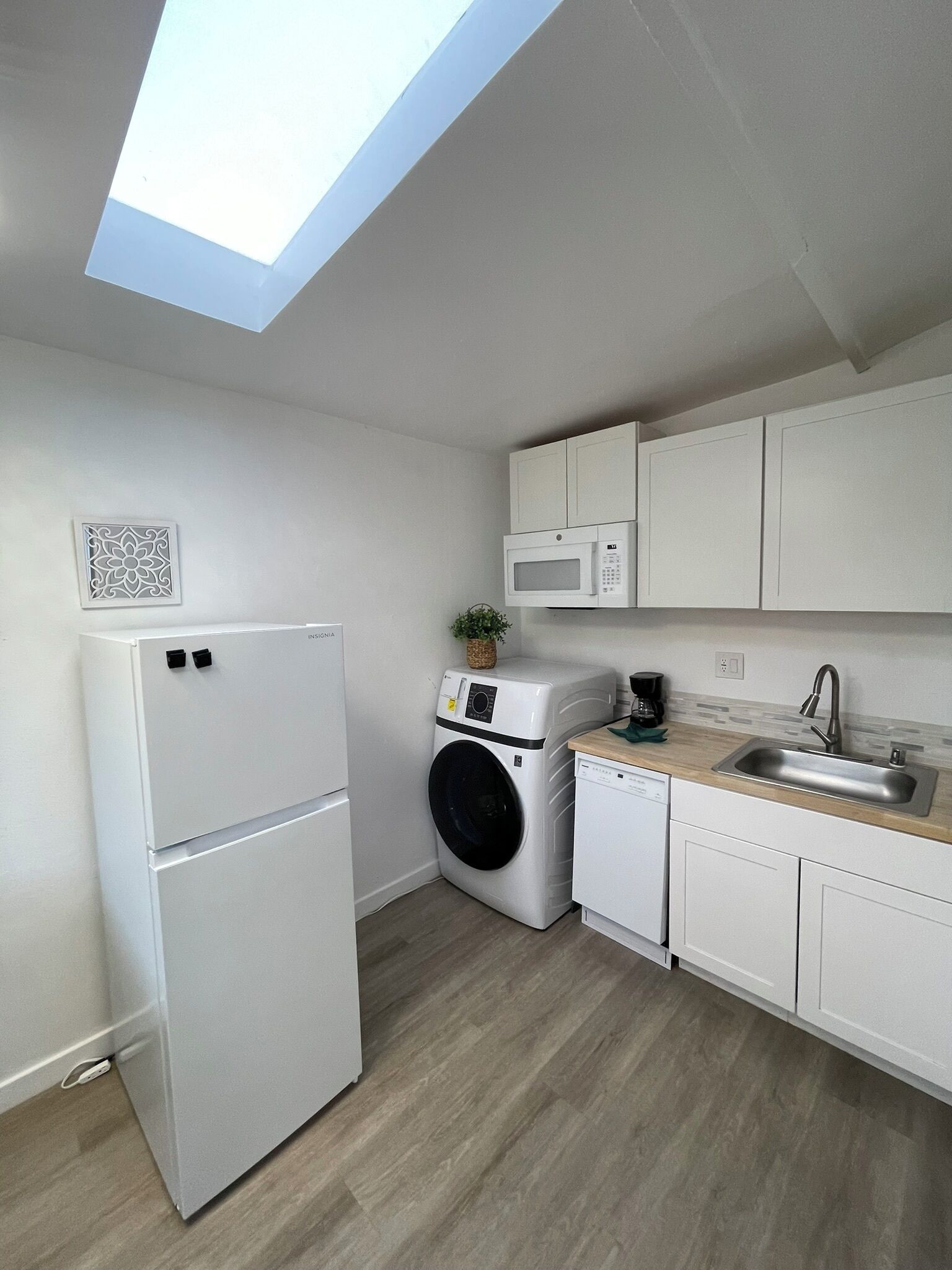 A compact kitchen with a washing machine, a microwave, and a refrigerator.