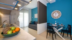 A modern kitchen with a dining area, featuring a green fruit bowl, a clock, and a dining table with chairs. - City Centre Gem in Chania (Χανιά)