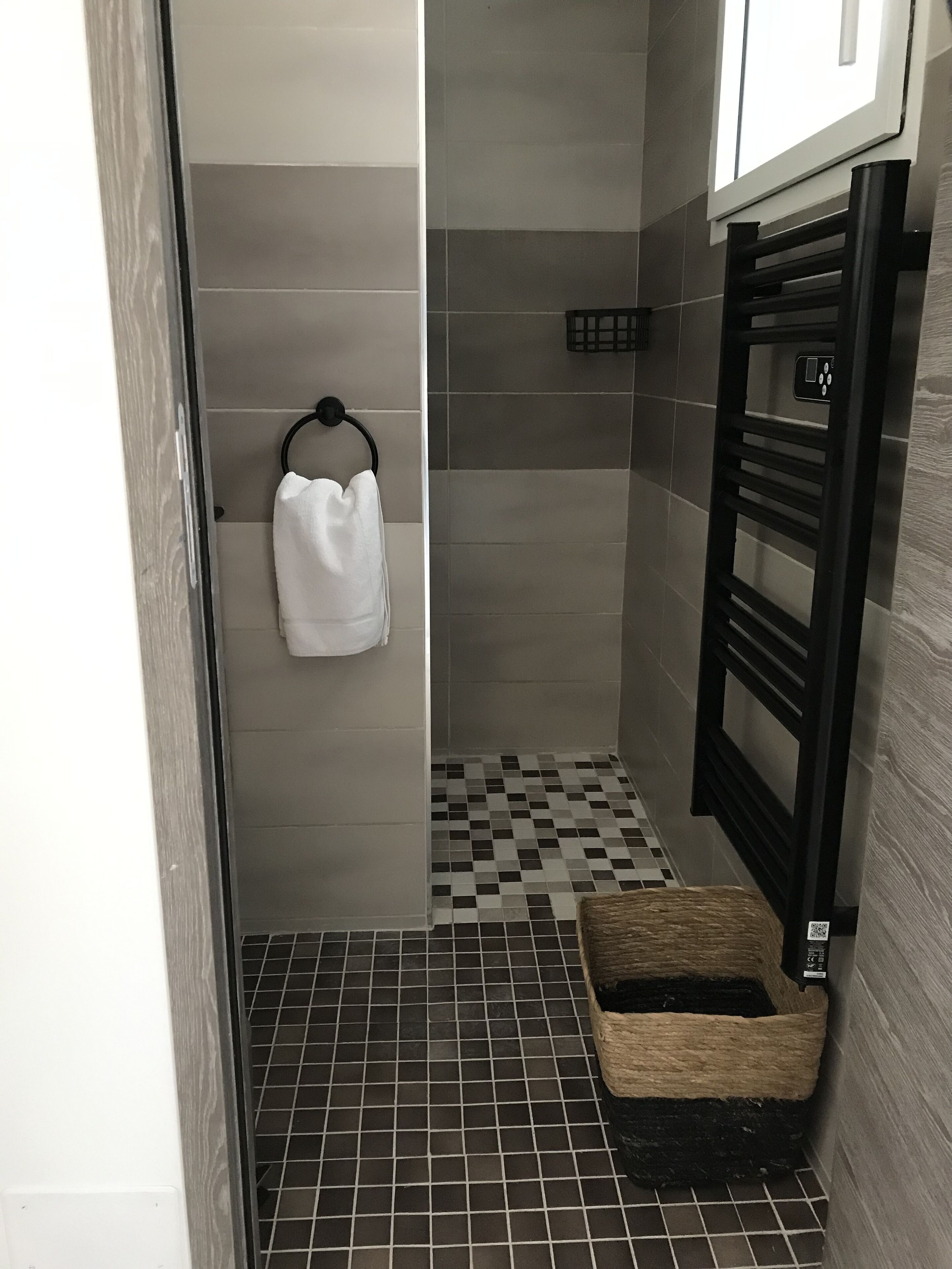 Un baño con piso a cuadros, un perchero con una toalla blanca, un perchero negro y una pequeña cesta de mimbre.