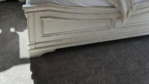 Et soveværelse med en polstret sengegavl, en seng med hvide sengetæpper, flere puder, et natbord med en lampe og et vindue med udsigt.