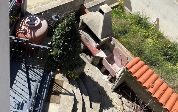 Una azotea con una maceta grande de terracota, una barandilla metálica y una estructura de hormigón con techo rojo.