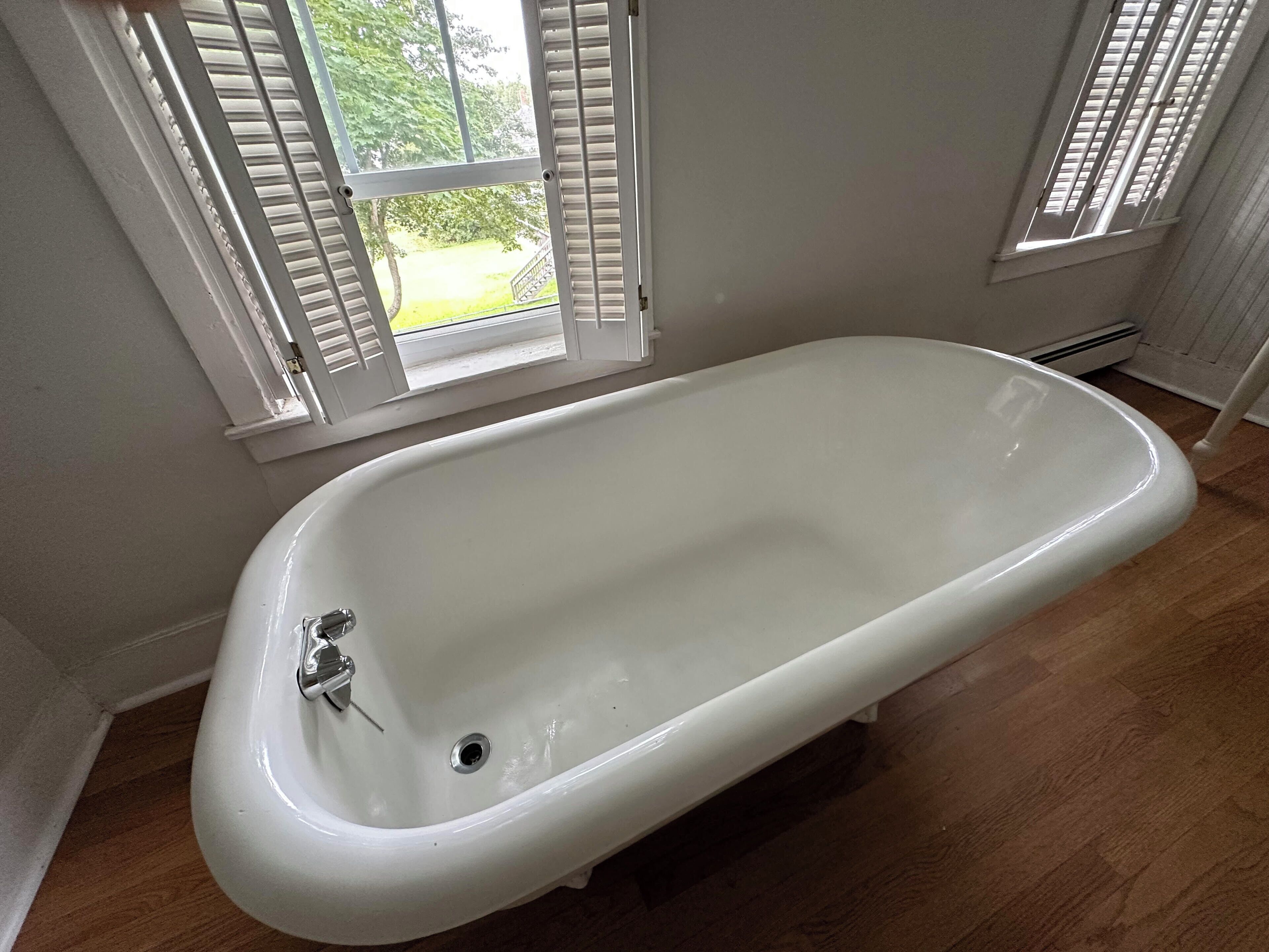 Eine weiße freistehende Badewanne in einem Badezimmer mit Holzboden und weißen Wänden.