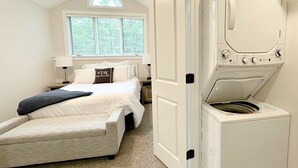 Une chambre à coucher avec un lit, un lave-linge et une fenêtre avec des stores.