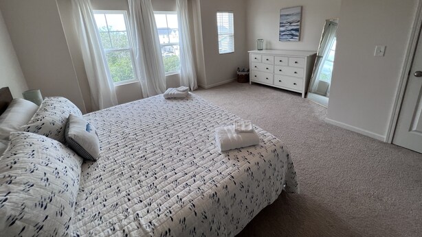 A bedroom with a large bed, a dresser, and a window with curtains.