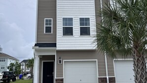 A two-story residential building with a garage, a driveway, and a palm tree.