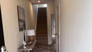 A hallway with a staircase, a bench with a lamp, and a door.