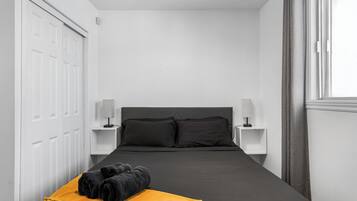 Un dormitorio con una cama negra, mesitas de noche blancas, un cabecero negro y una manta amarilla.