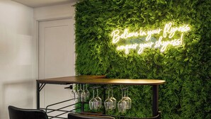 A bar area with a green wall, a neon sign, and a wooden table with chairs.