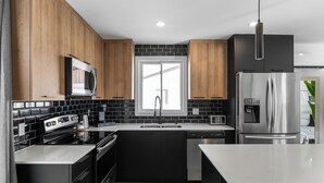A modern kitchen with black and wooden cabinets, stainless steel appliances, and a large window.