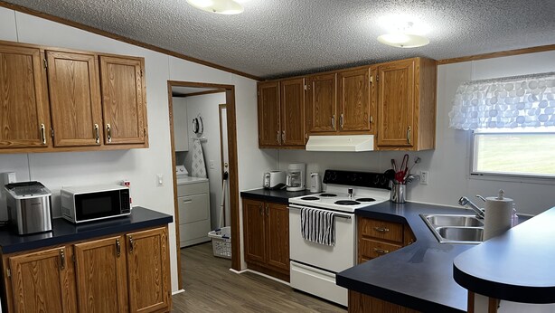 A compact kitchen with wooden cabinets, a microwave, a stove, and a sink. - Kim's Place (Cookeville)