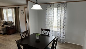 A dining area with a dark wooden table and chairs, a hanging light fixture, and patterned curtains. - Kim's Place (Cookeville)
