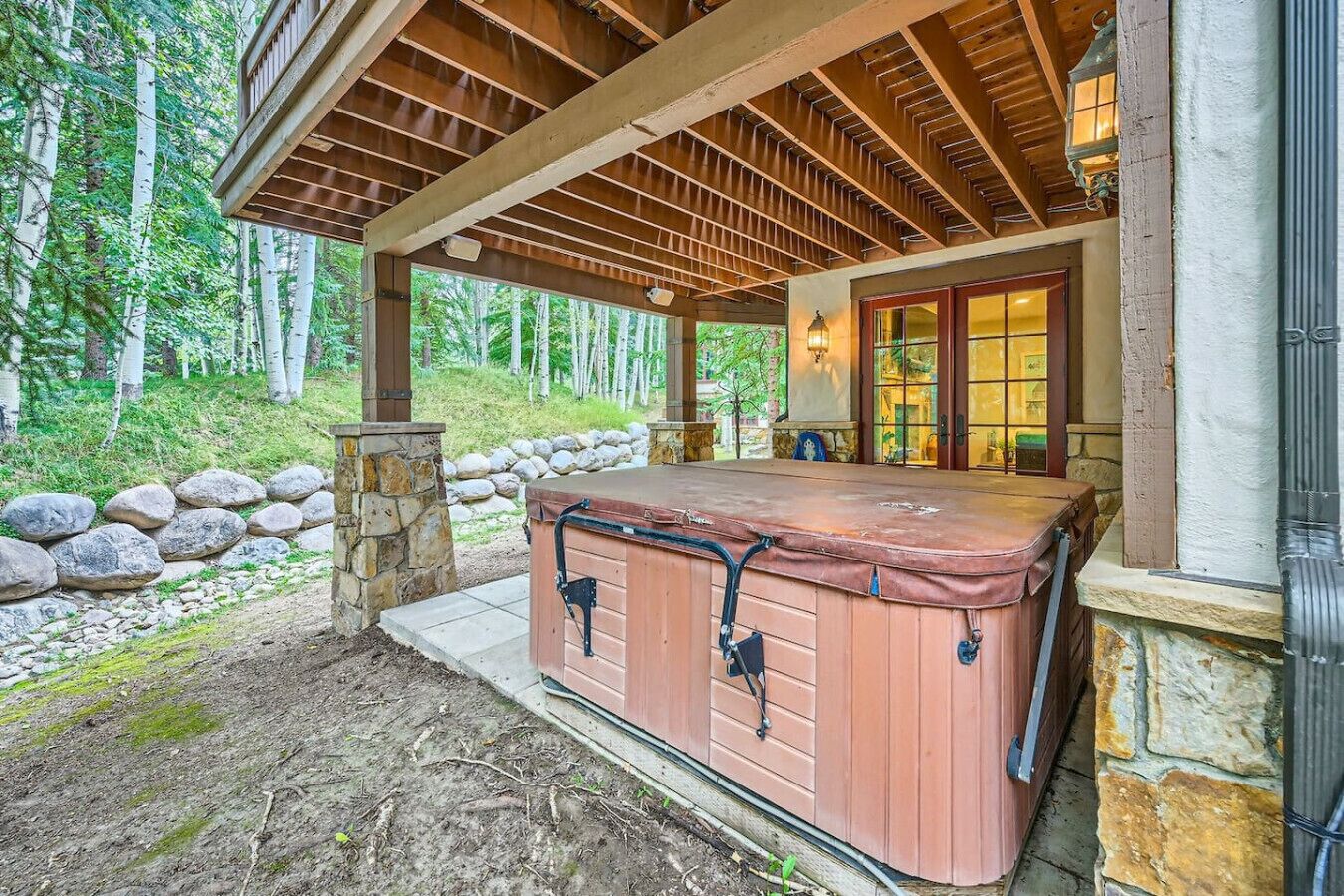 A hot tub under a wooden pergola, surrounded by a stone wall and a stone staircase.