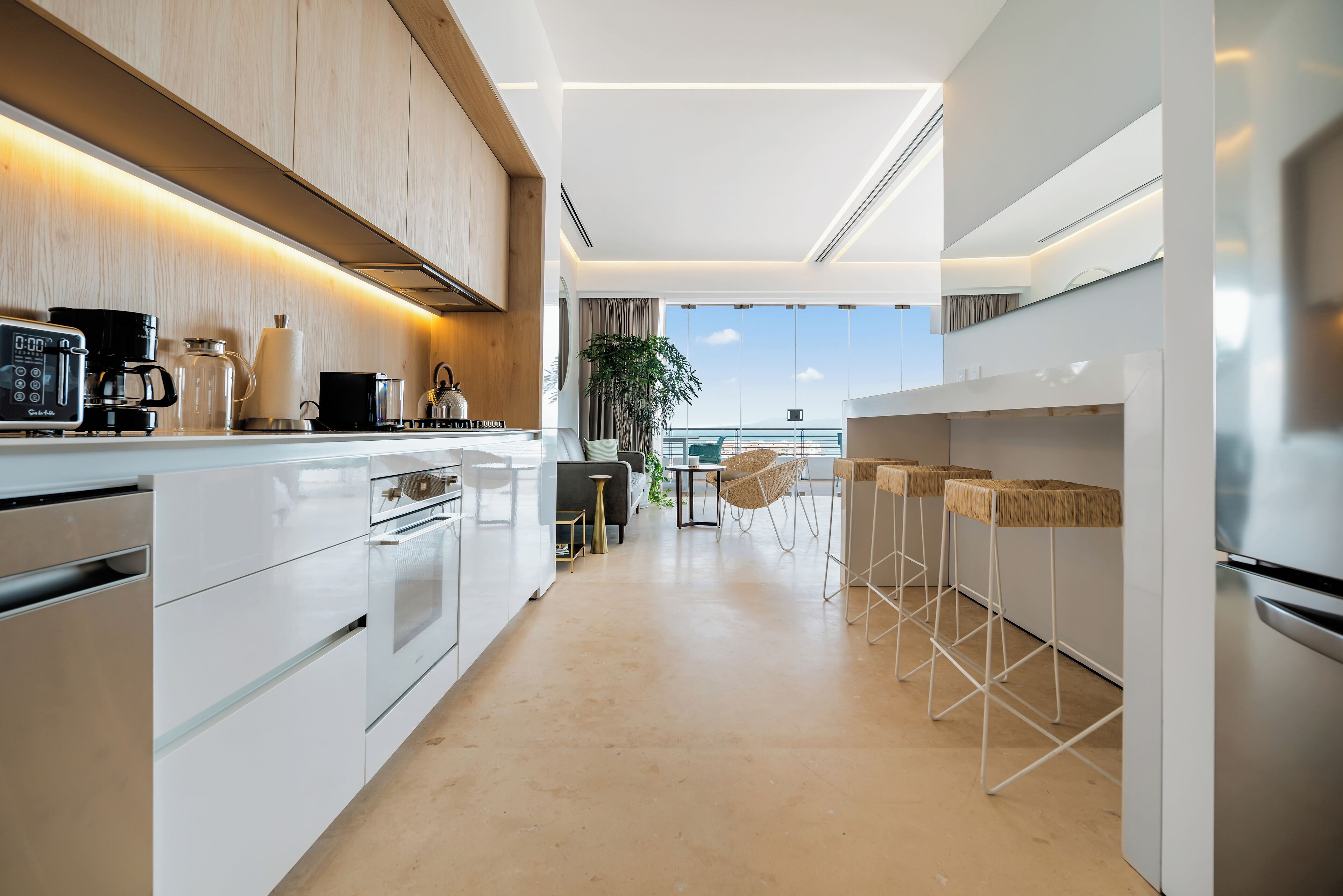 A modern kitchen with white cabinetry, a coffee machine, and a view of the ocean.