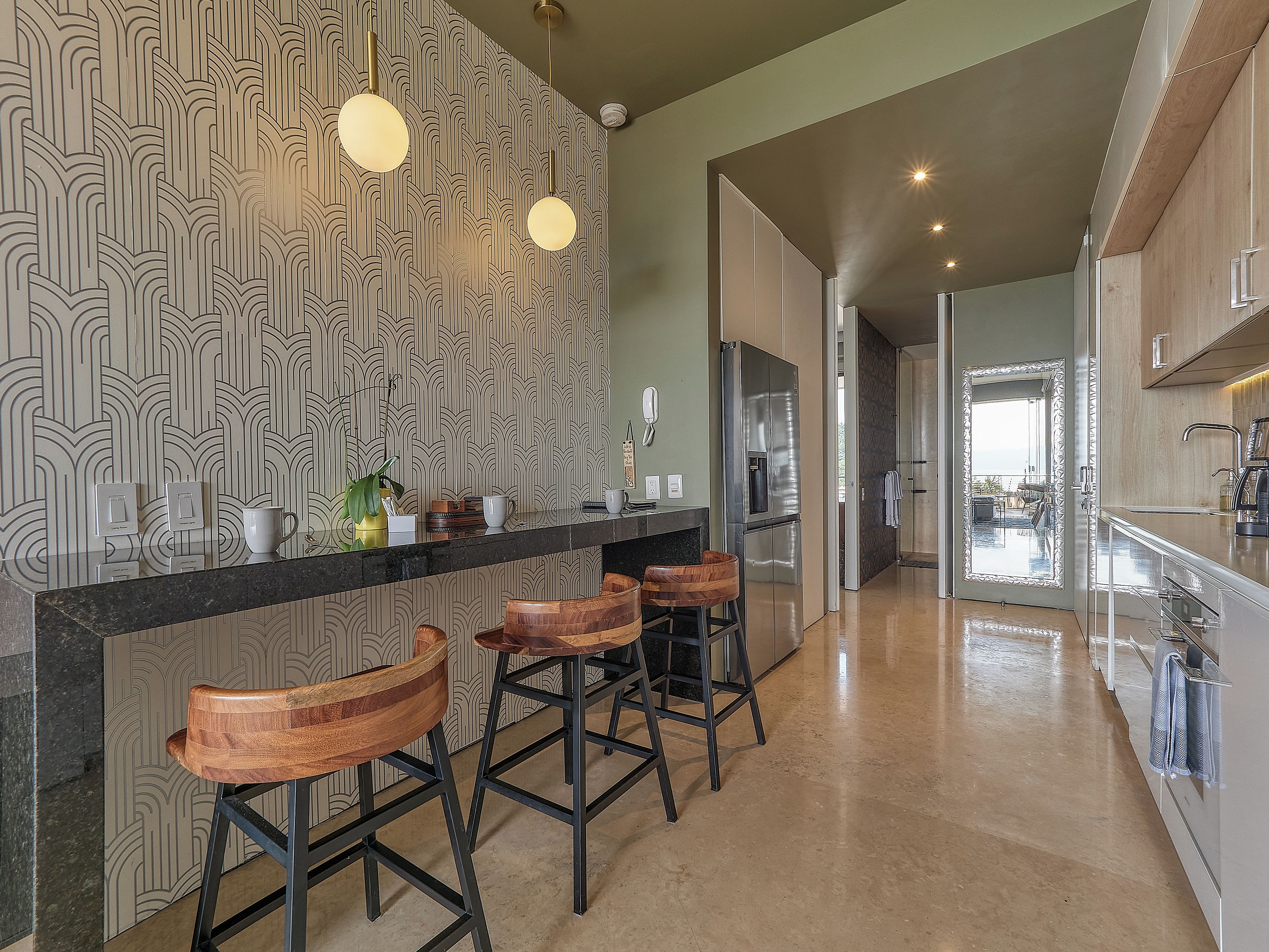 A modern kitchen with a patterned backsplash, stainless steel appliances, and wooden bar stools.