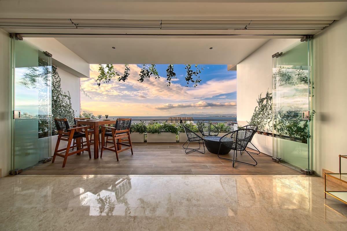 Un balcon moderne avec une table et des chaises en bois, des murs en verre et une vue sur la mer.
