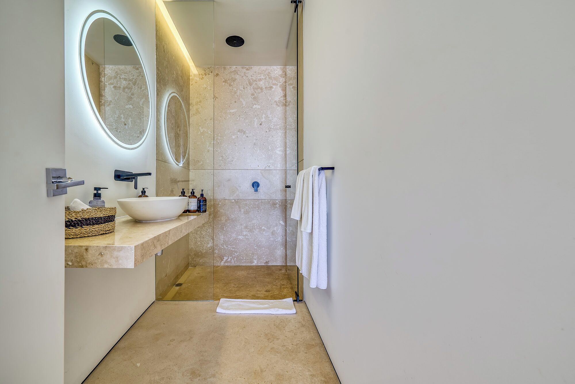 Un bagno moderno con un grande specchio ovale, un lavabo a incasso e uno spazio doccia in vetro.