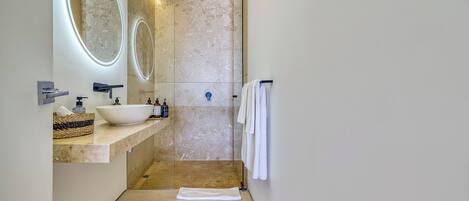 Un bagno moderno con un grande specchio ovale, un lavabo a incasso e uno spazio doccia in vetro.
