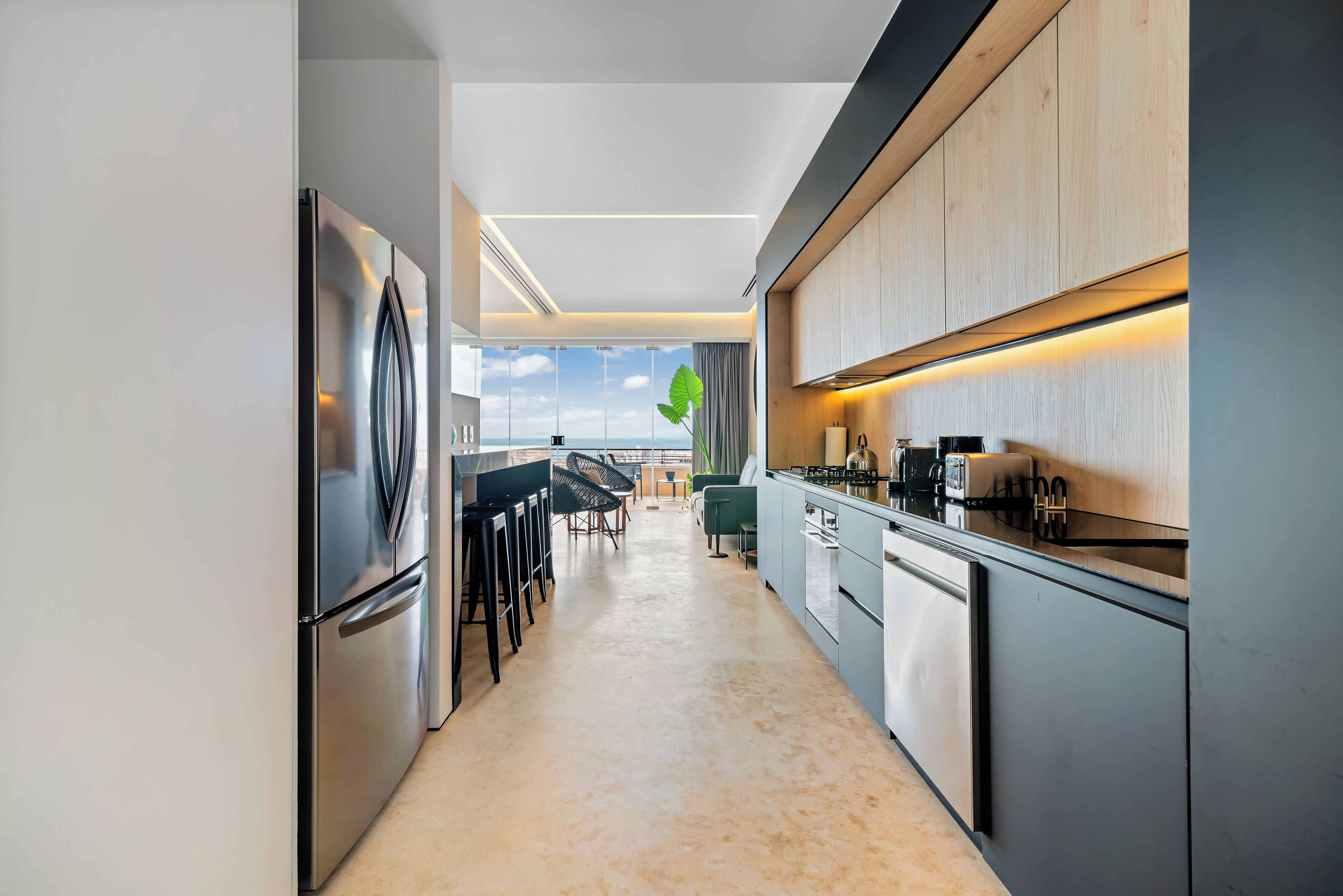 Una cocina moderna con un refrigerador de acero inoxidable, taburetes de bar y vistas al cielo.