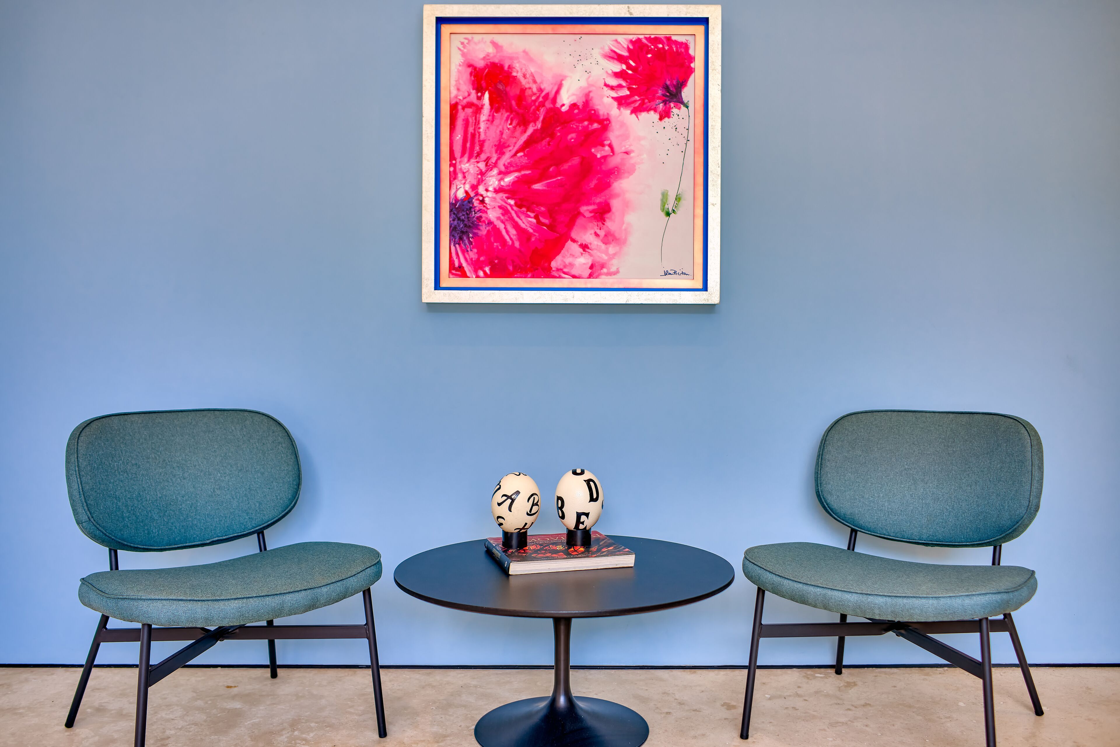 Two chairs with a table between them, a framed artwork above, and two decorative objects on the table.
