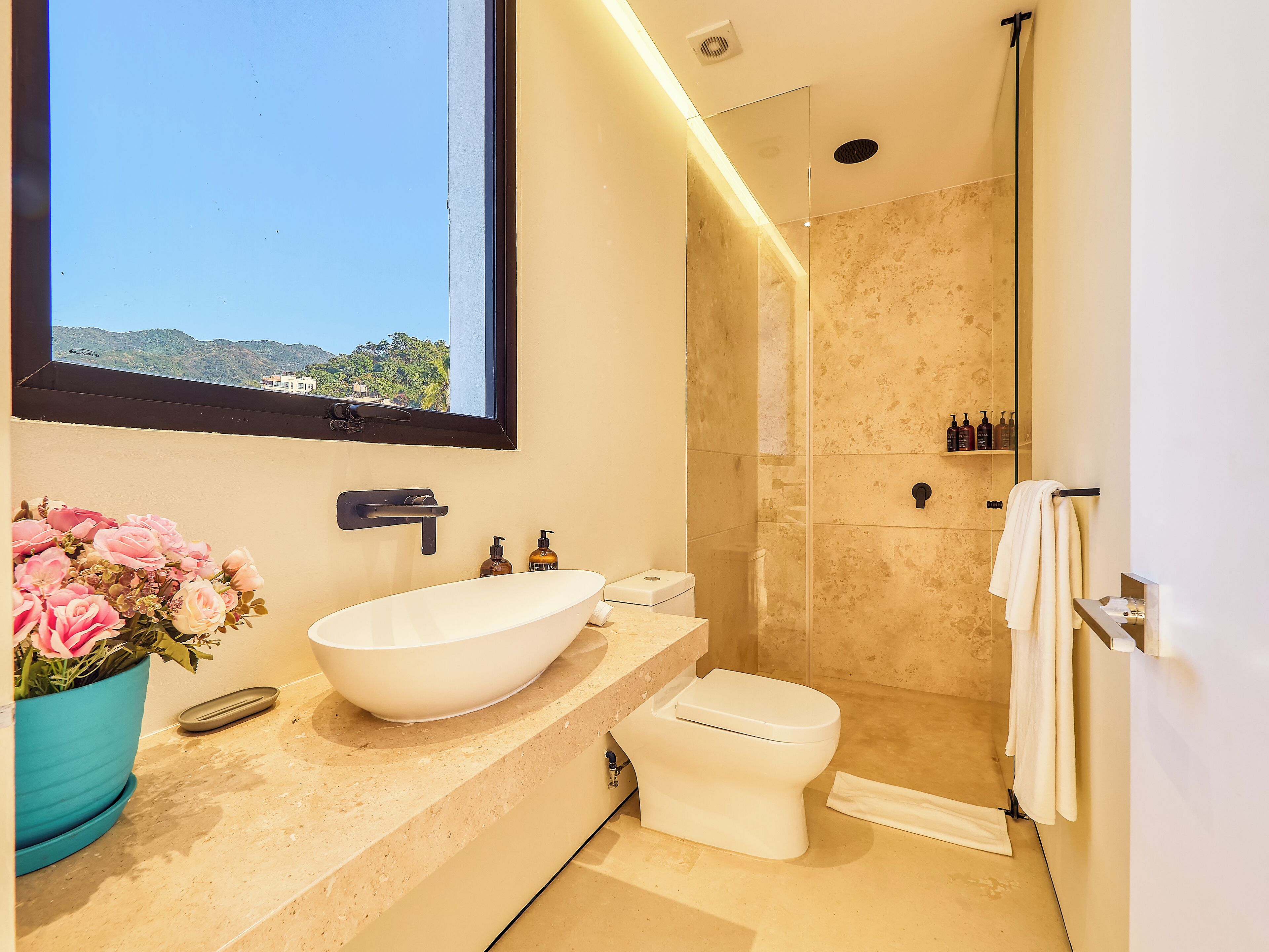 Ein modernes Badezimmer mit großem Fenster, Waschbecken in Weiß, Toilette und Duschbereich.
