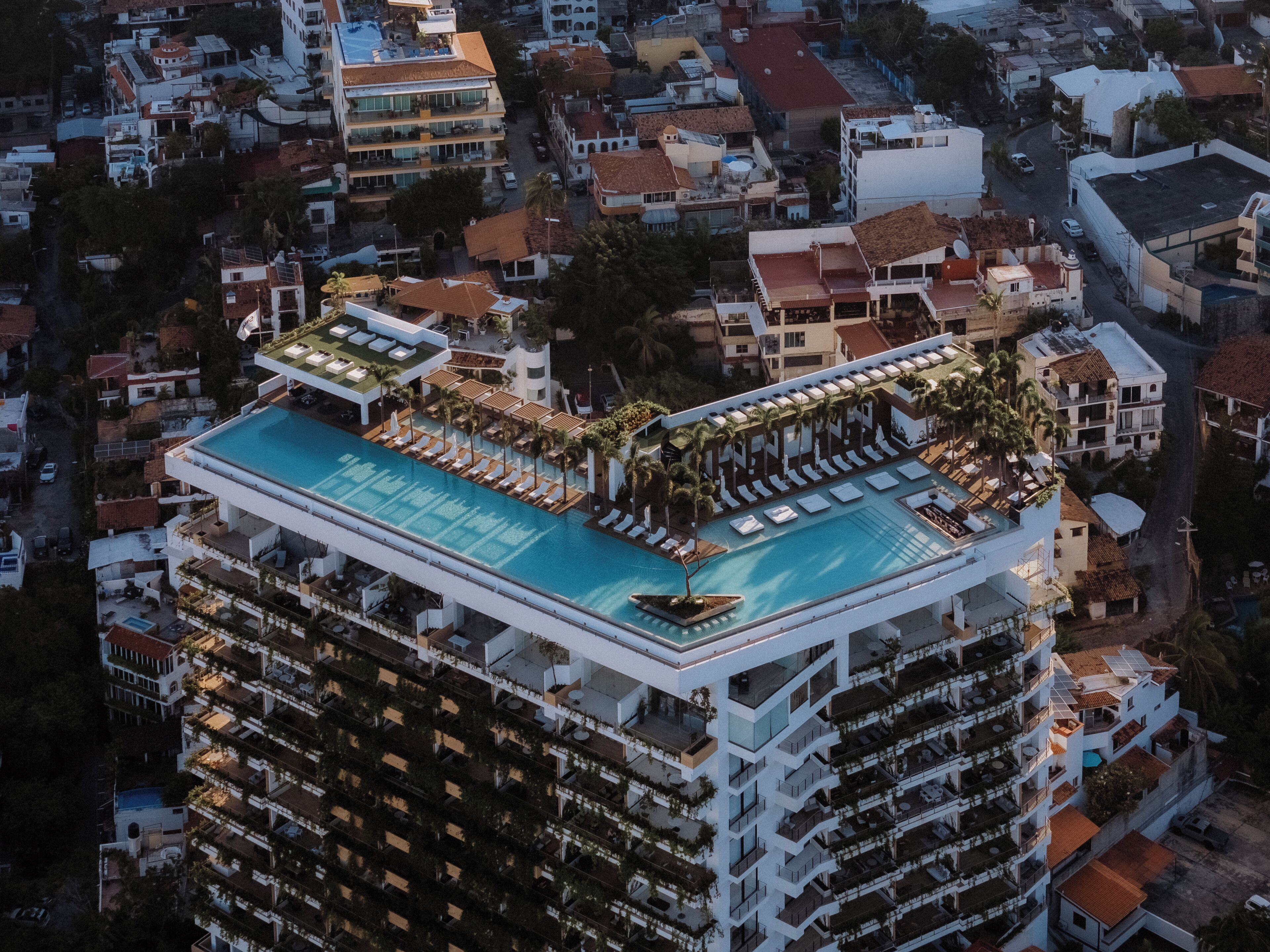 Un hotel moderno de gran altura con piscina en la azotea, varios balcones y un diseño arquitectónico contemporáneo.