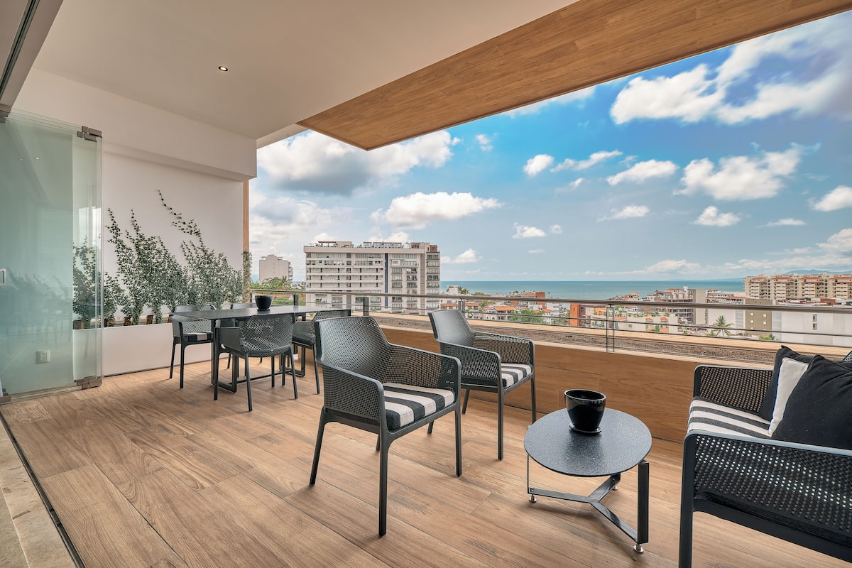 Un balcon doté d’un plancher en bois, de meubles en rotin noir et offrant une vue sur la ville et la mer.