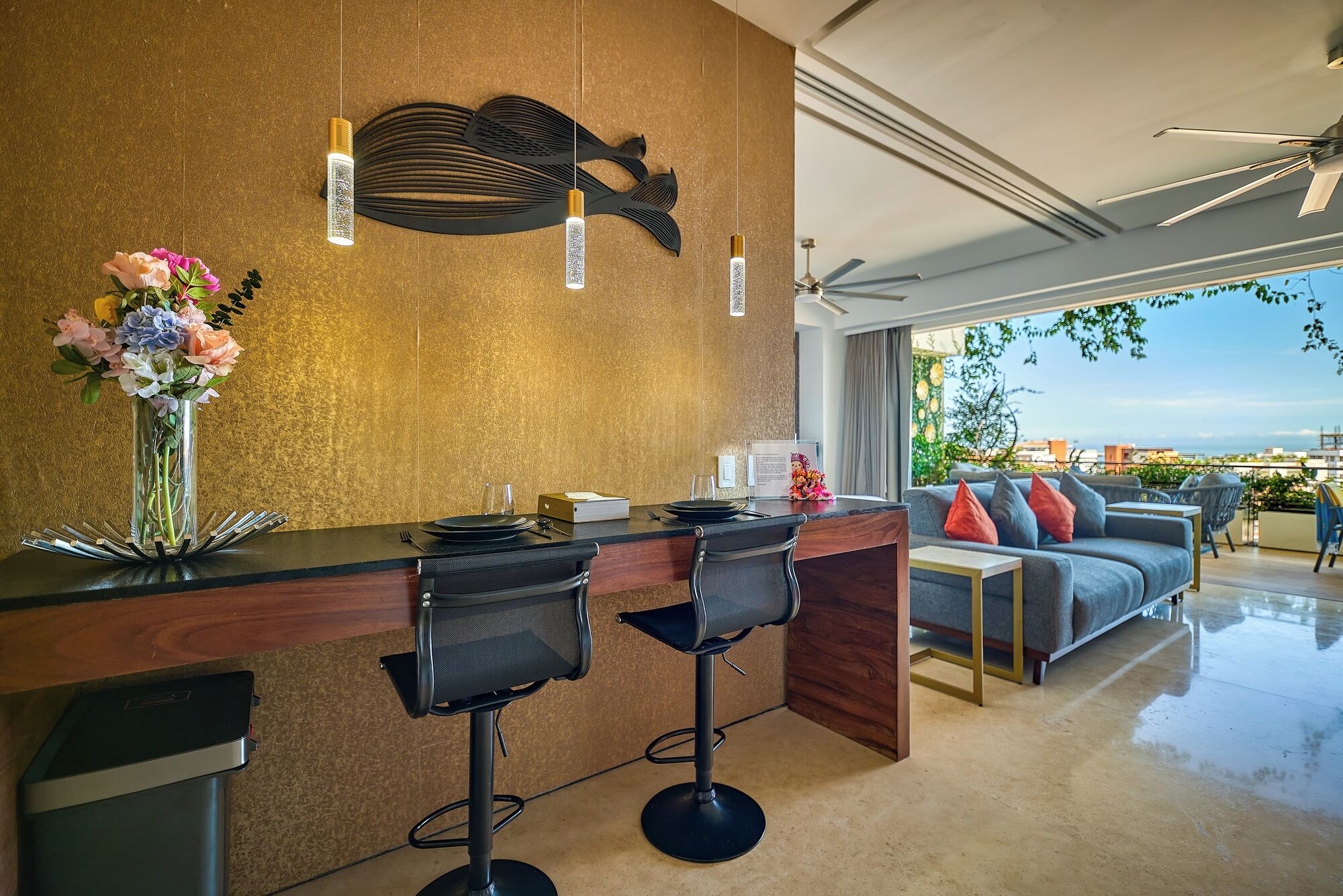 Un espace de restauration moderne avec un bar, deux tabourets de bar, un vase de fleurs et une vue sur la ville.