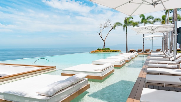Un espace aménagé au bord de la piscine, avec des chaises longues et une vue sur l’océan.