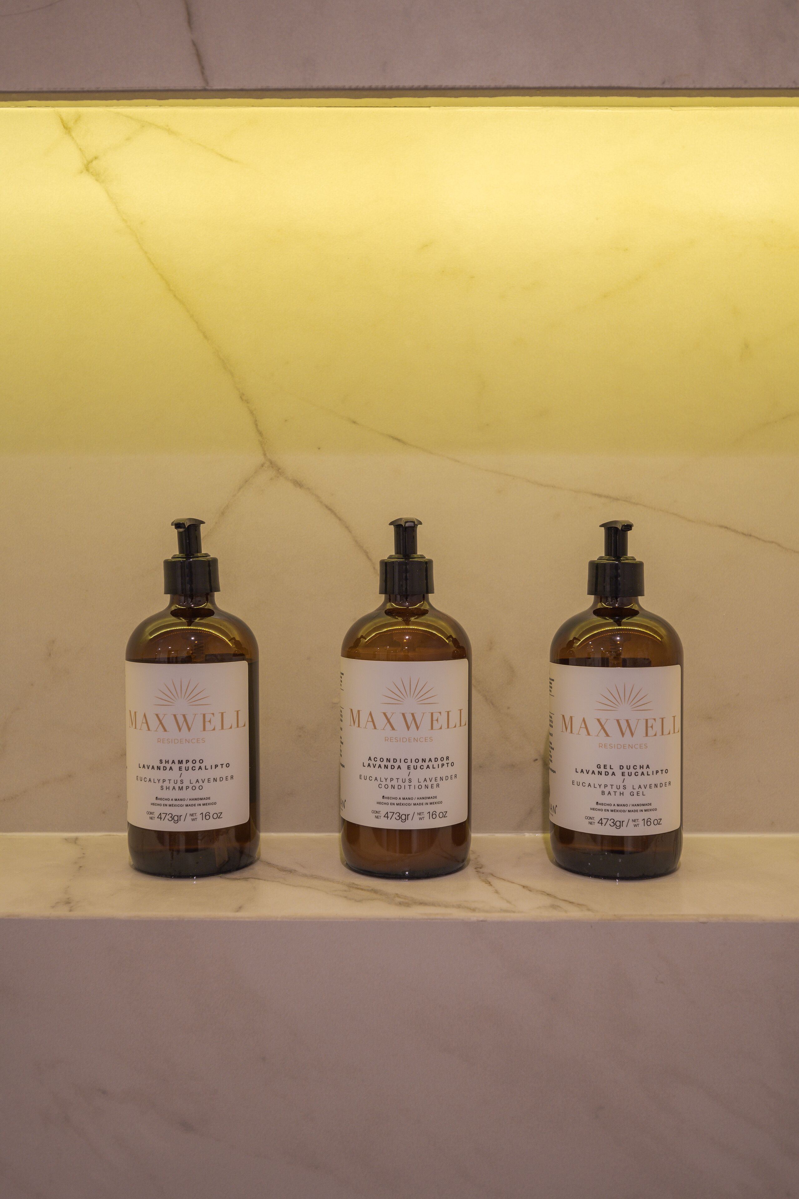 Drie flessen MAXWELL shampoo en conditioner op een marmeren plank.