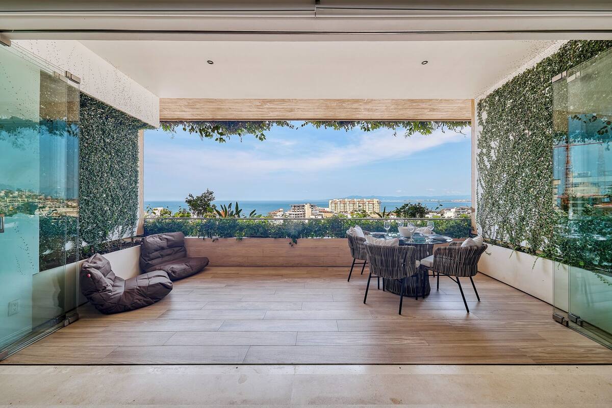 Une terrasse extérieure moderne, dotée d’un plancher en bois, d’un espace salon avec un banc rembourré et d’une table à manger avec des chaises.