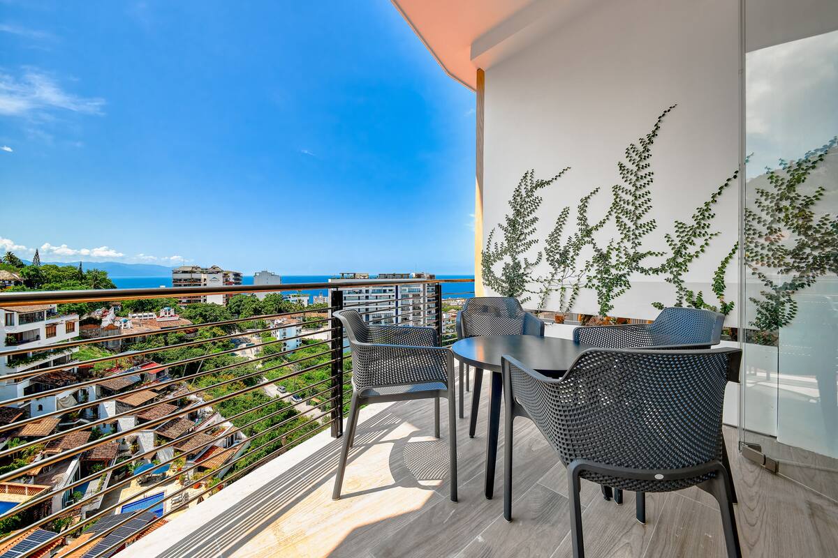 Un balcon avec une table et des chaises, offrant une vue sur le paysage urbain et la mer.