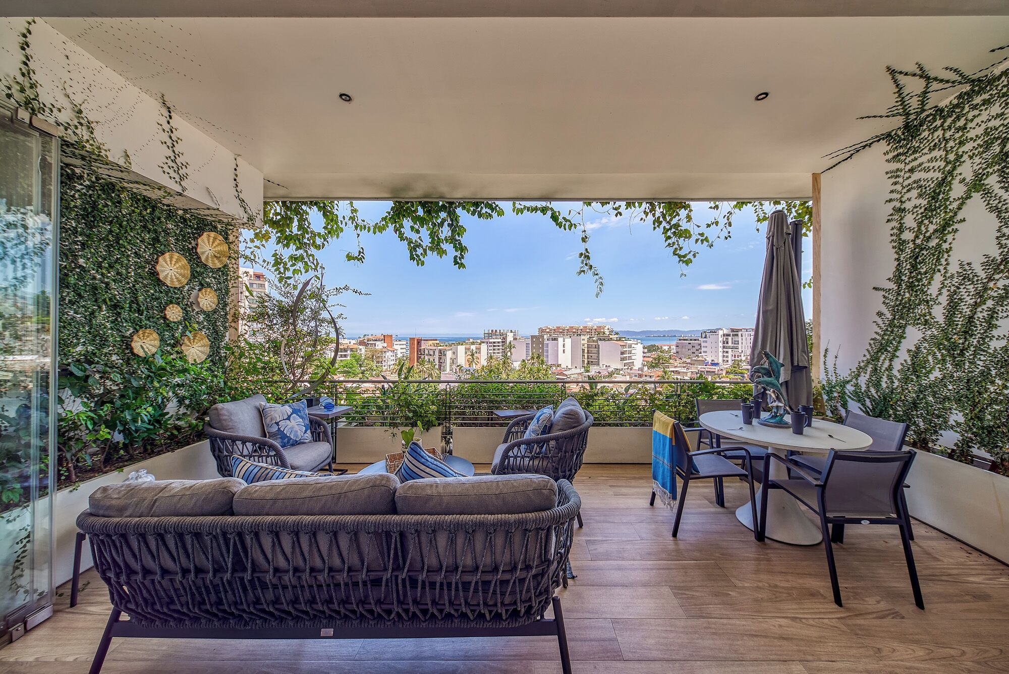 Een balkon met rieten meubels, een ronde tafel en uitzicht op de stad.