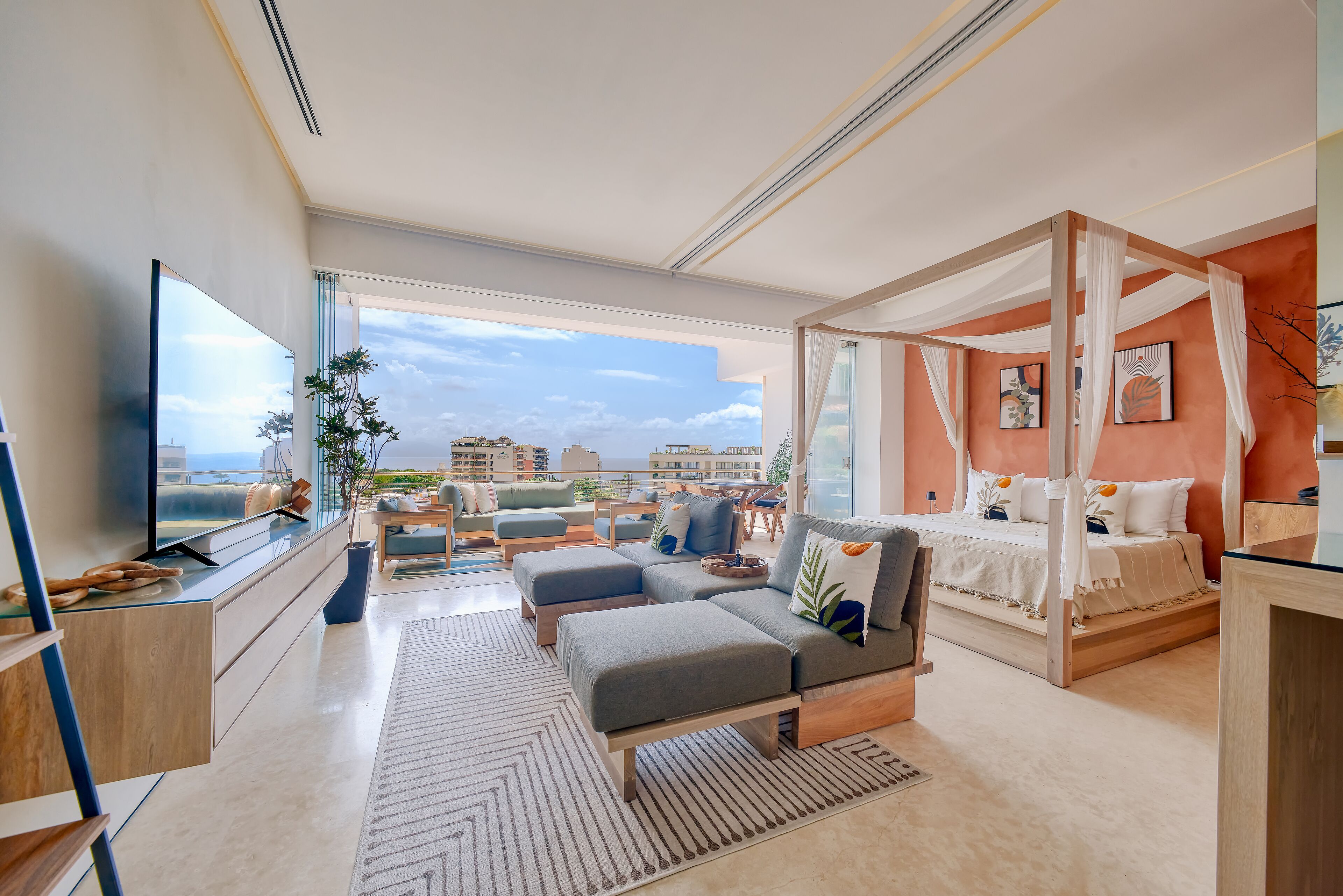 Una sala de estar moderna con un televisor grande, asientos cómodos, una cama con dosel y vistas a la ciudad.