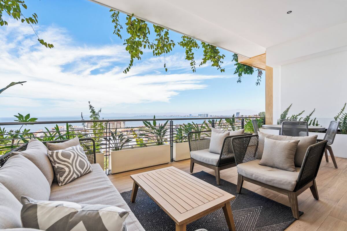 Un balcon aménagé avec un canapé, des chaises et une table, offrant une vue sur le paysage urbain et la mer.