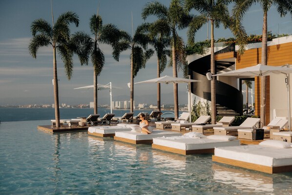 Un espace aménagé au bord de la piscine, avec des chaises longues et une femme assise sur une plateforme.