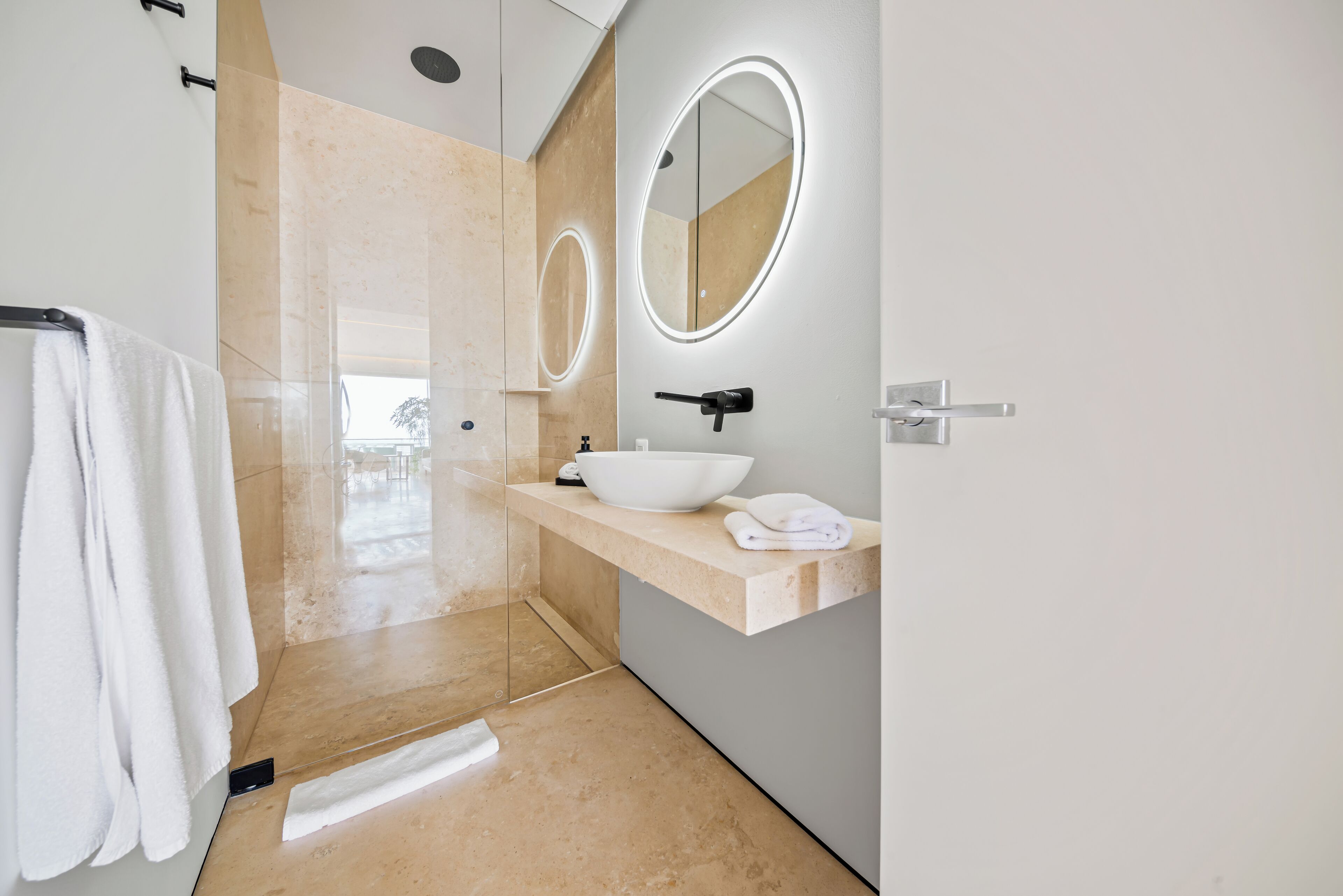 A modern bathroom with a large mirror, a white sink, and a glass shower enclosure.