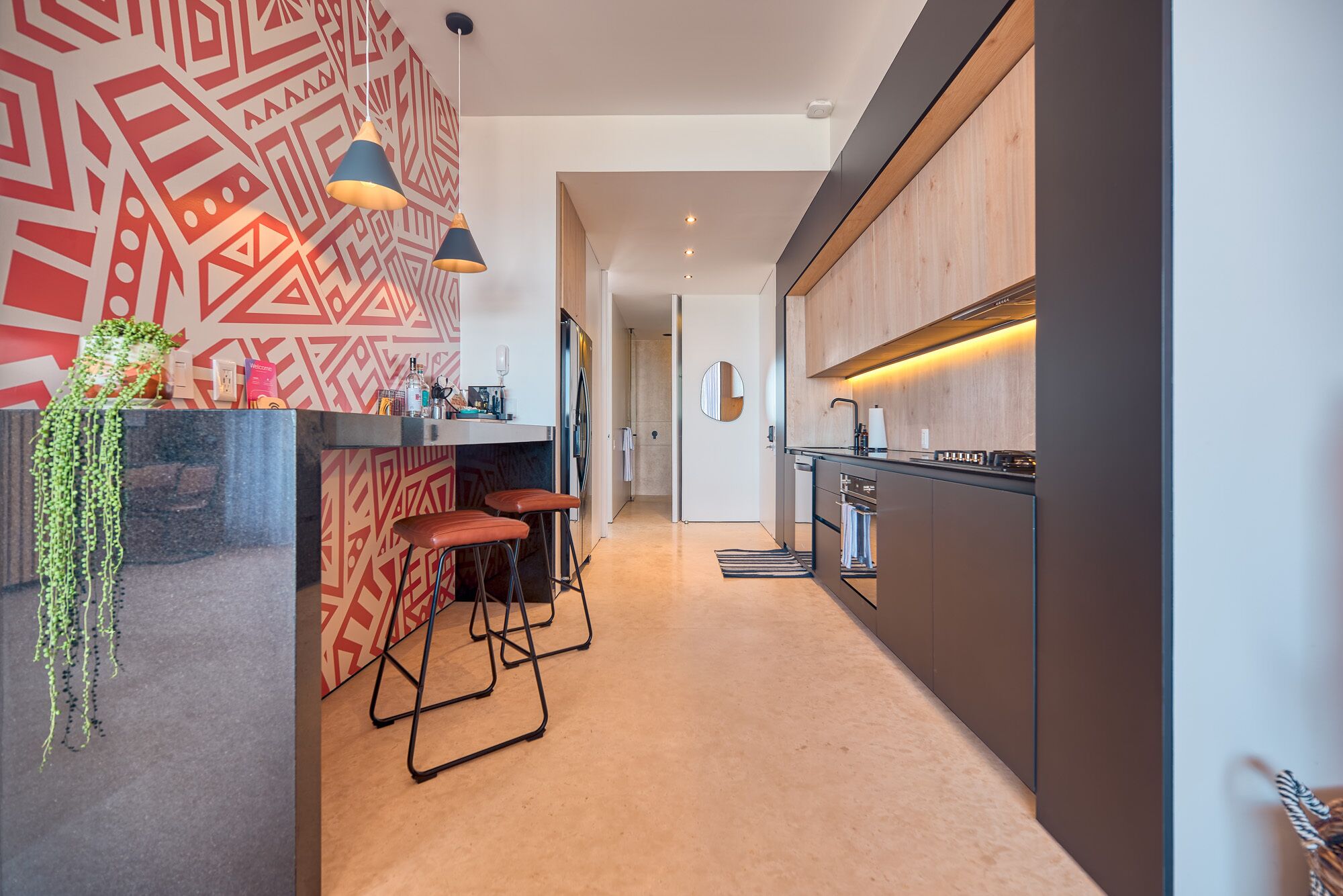 A modern kitchen with a central island, bar stools, pendant lighting, and a wooden backsplash.