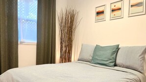 Ein Schlafzimmer mit einem Bett, einem Fenster mit Vorhängen und zwei gerahmten Bildern an der Wand.