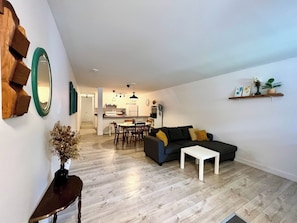 A modern living room with a sofa, coffee table, and a dining area with chairs and a table. - Apartment in Limoilou (Québec)