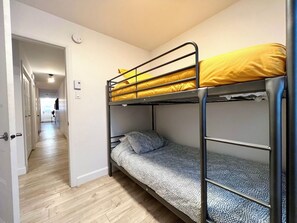 A bunk bed with a lower bunk and a single bed, both with patterned bedding. A door leads to a hallway. - Apartment in Limoilou (Québec)