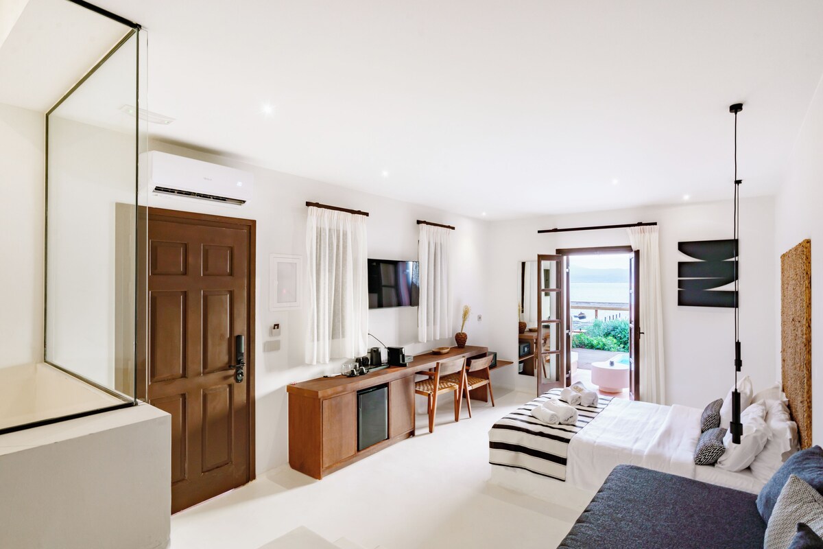 Quarto de hotel moderno com uma escrivaninha de madeira, uma cama, uma televisão e vista para o exterior.