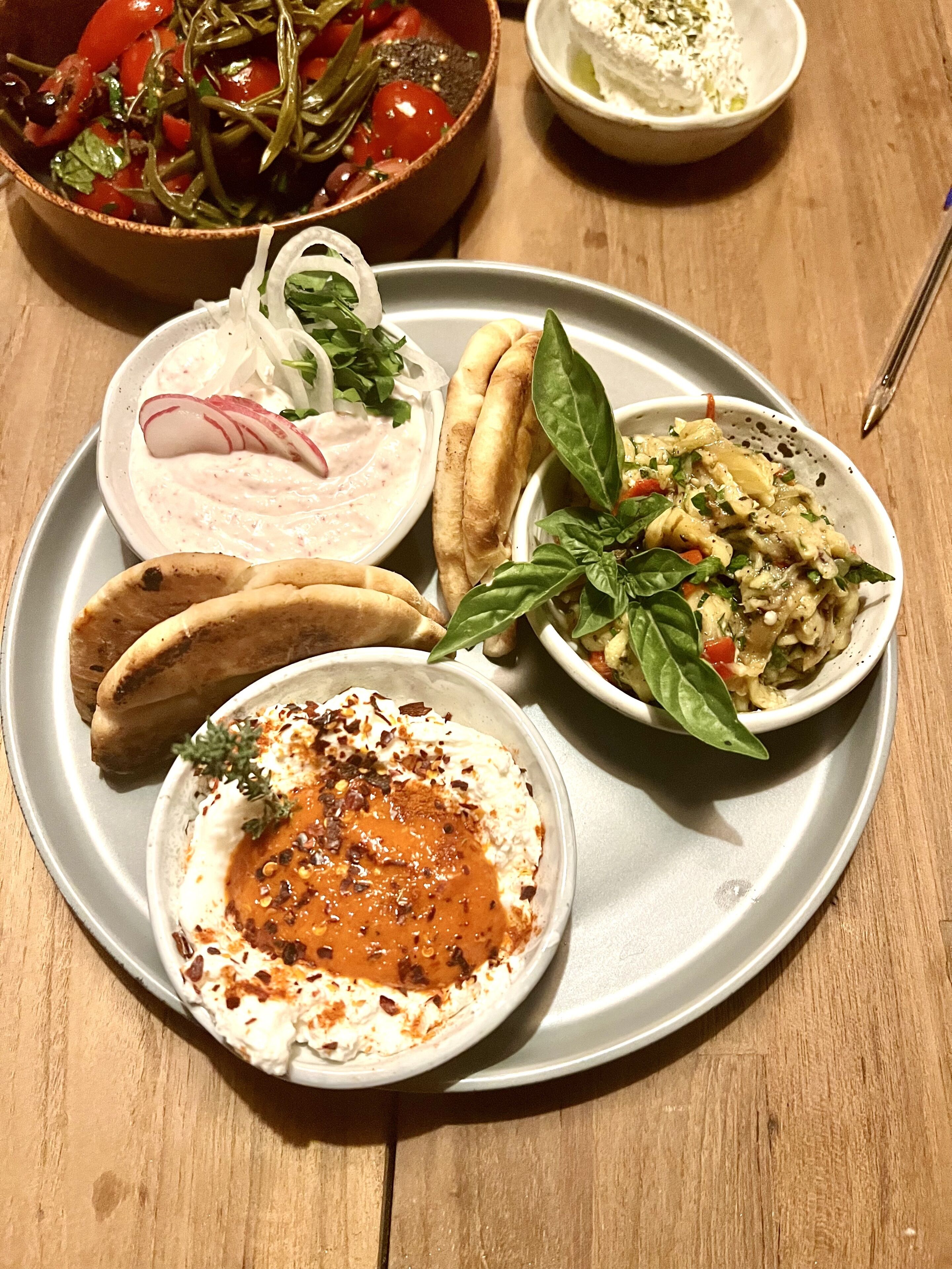 A plate with various dishes including a salad, a bowl of dip, pita bread, and a bowl of pasta.