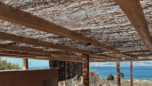 Un área de estar al aire libre con mobiliario de madera y techo de paja, con vista a una piscina y al mar.