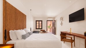 Une chambre moderne avec un grand lit, un bureau en bois, une télévision et une vue sur l’extérieur.
