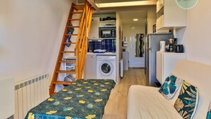Een ruimtelijk ingerichte leefruimte met een bed, een wasmachine, een magnetron en een koelkast.