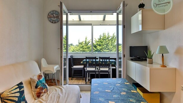 Een slaapkamer met een bed, een televisie, een bureau en een raam met uitzicht op groen.