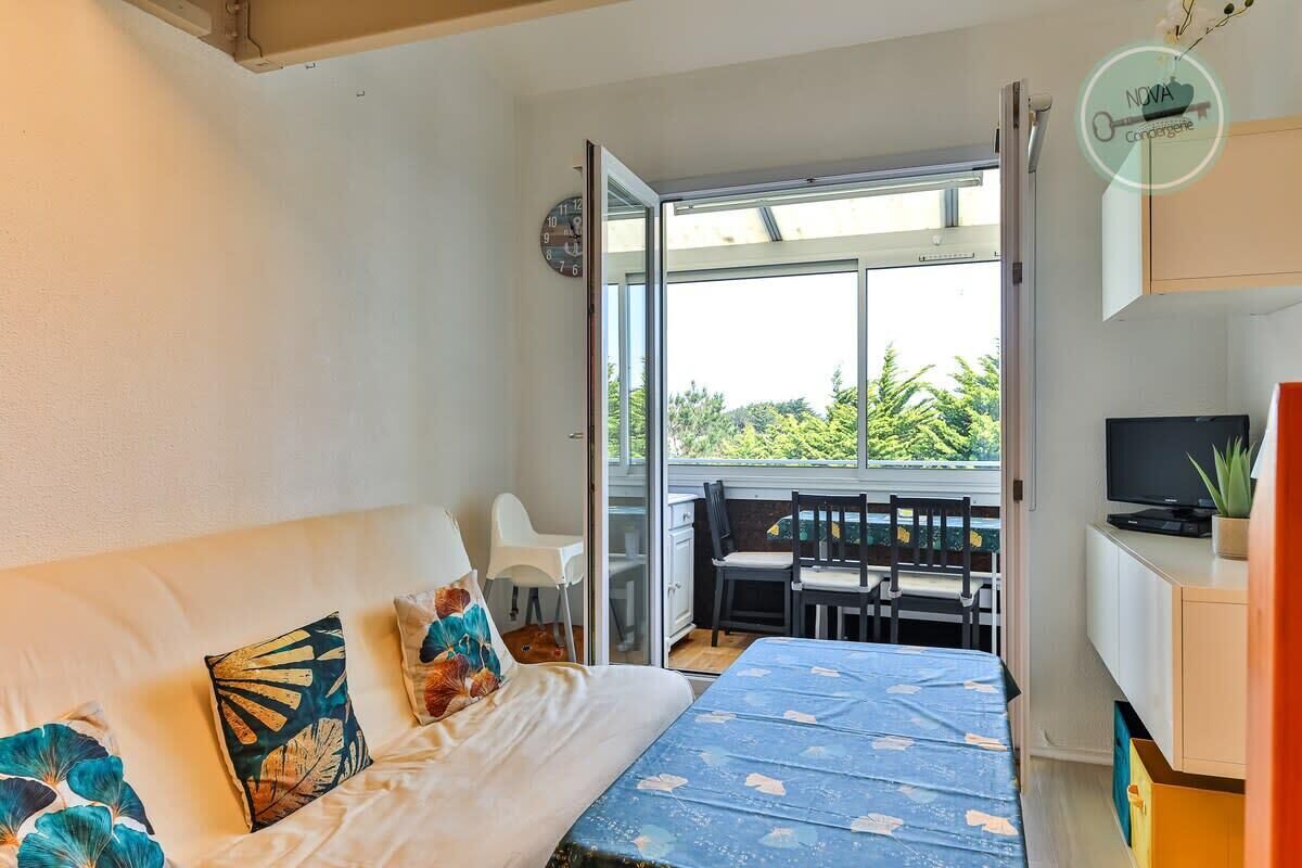 A bedroom with a bed, a TV, and a balcony with a view of greenery.