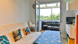 Een slaapkamer met een bed, een televisie en een balkon met uitzicht op groen.